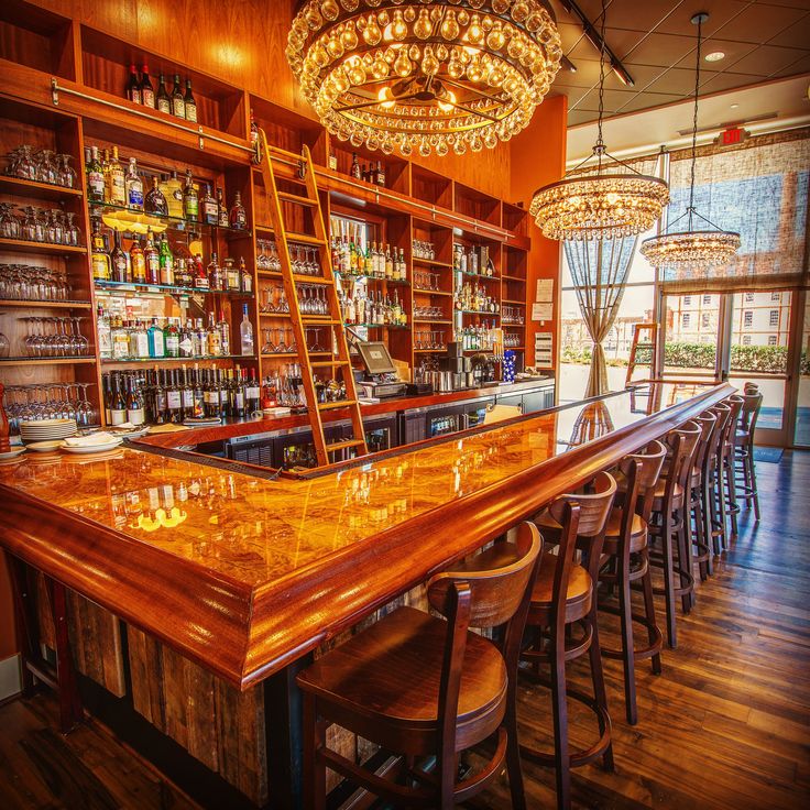 a bar with wooden shelves and stools in front of an open area that has lots of bottles on it