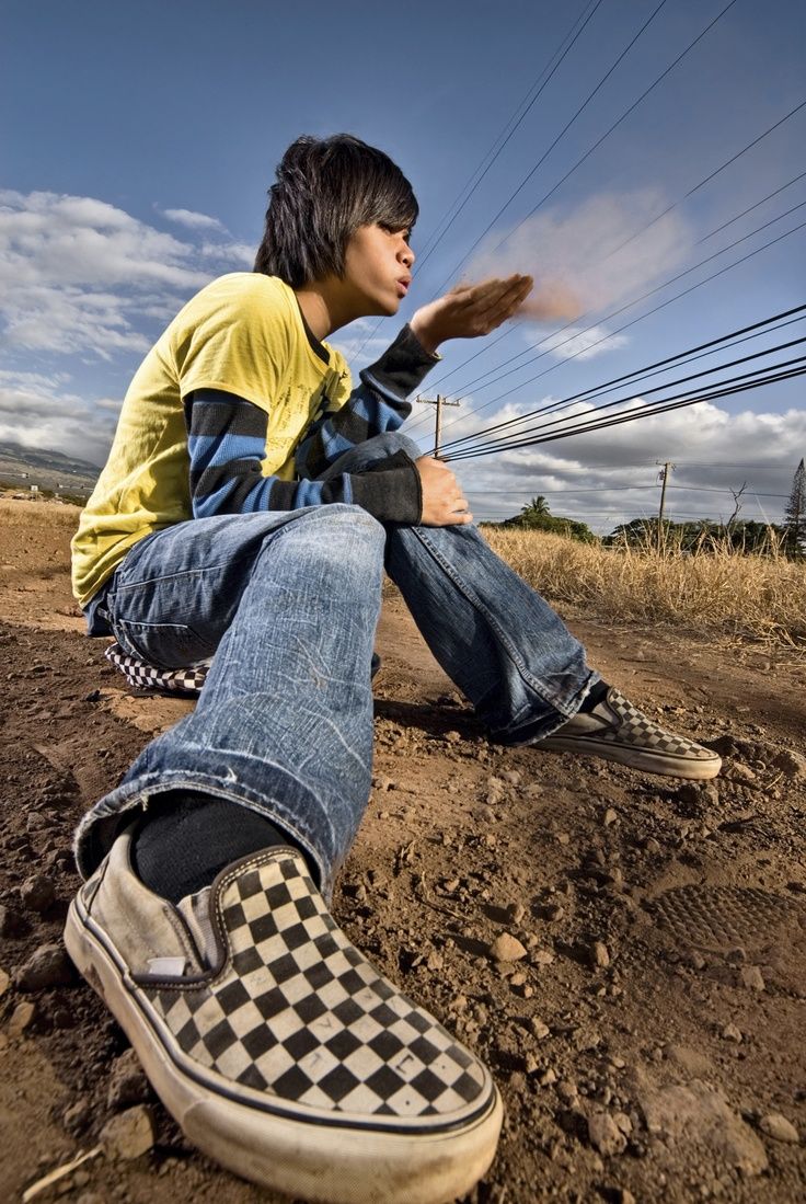 a young man sitting on top of a dirt field next to power lines and telephone poles