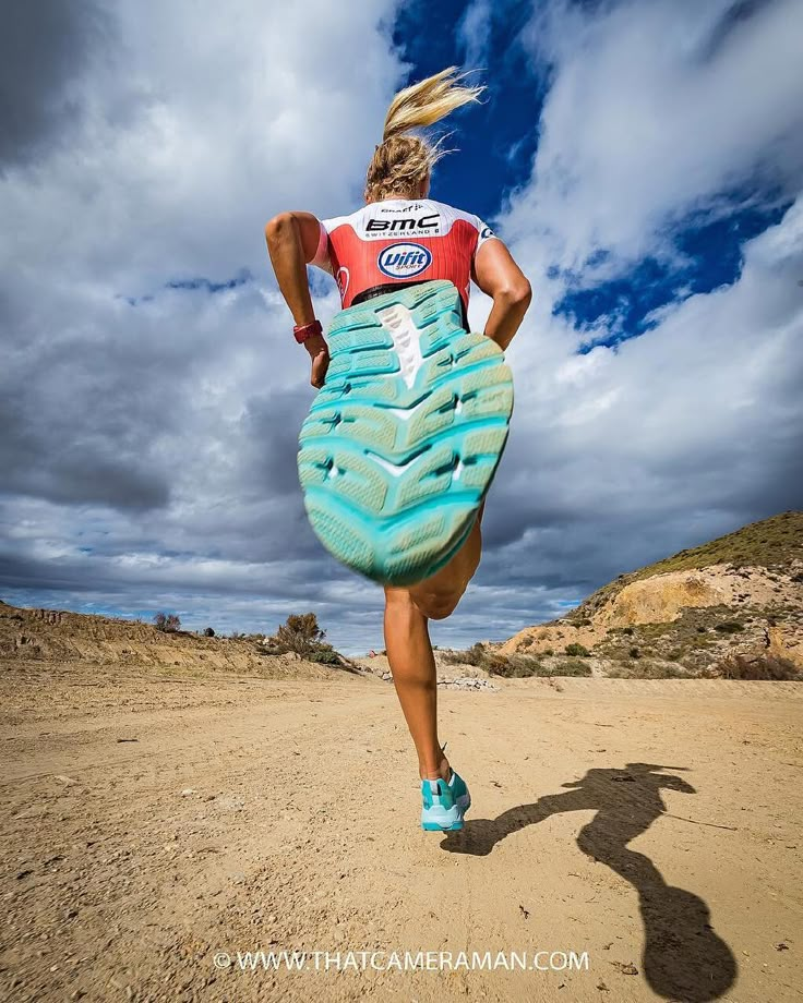 a woman running across a sandy beach under a blue sky with clouds in the background