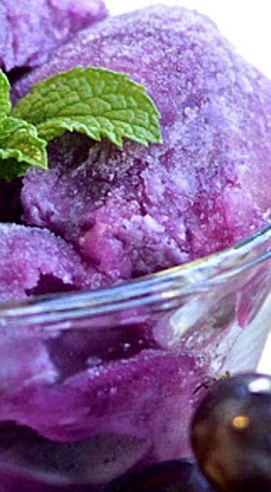 two scoops of blueberry ice cream in a glass bowl with mint leaves on top