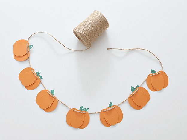 an orange string with paper pumpkins on it next to a roll of twine