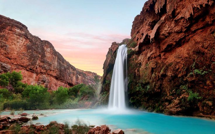 a large waterfall in the middle of a river surrounded by rocks and greenery at sunset