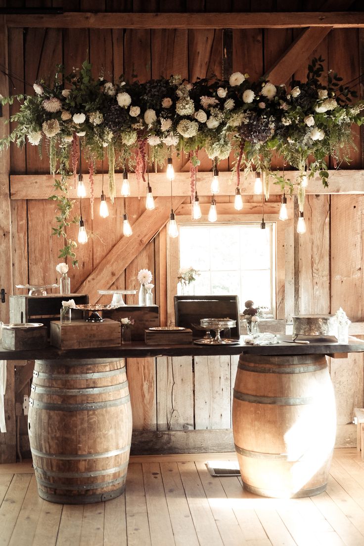 a wooden table topped with wine barrels filled with flowers and greenery next to a window