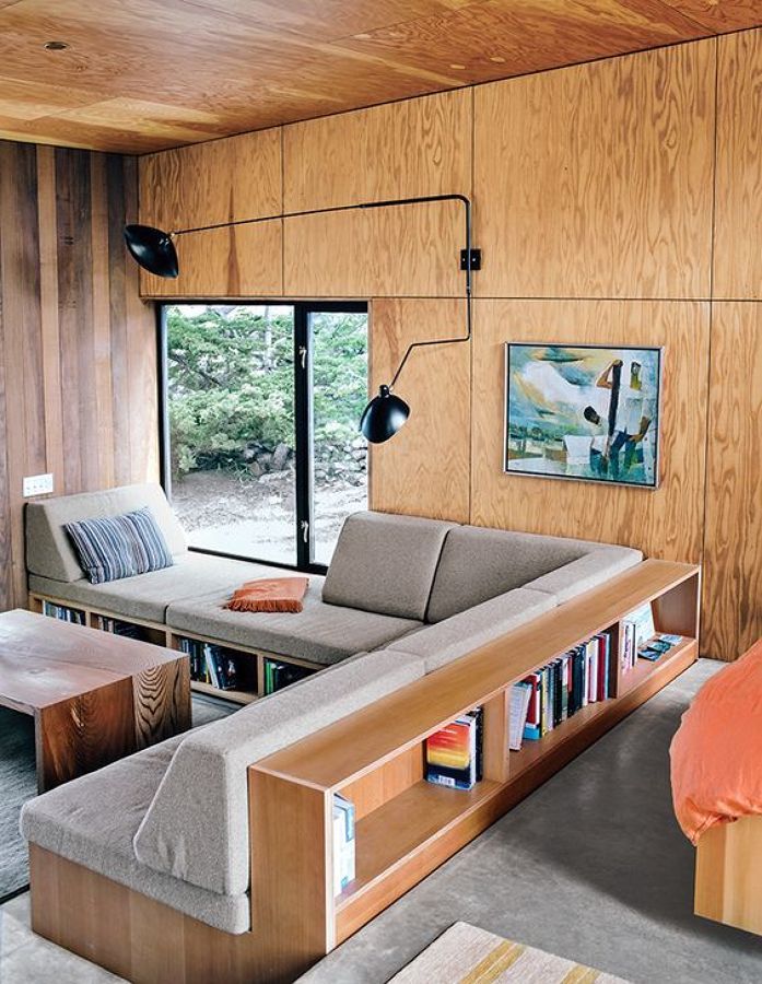 a living room filled with furniture next to a large glass window and wooden wall mounted bookshelf