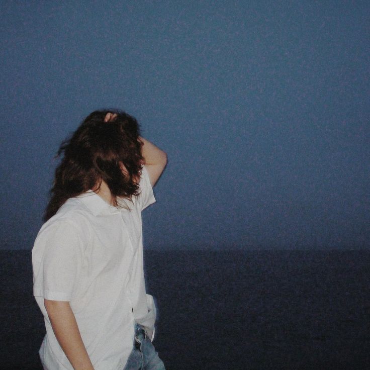 a man standing on the beach at night with his hair blowing in the wind and looking out to sea