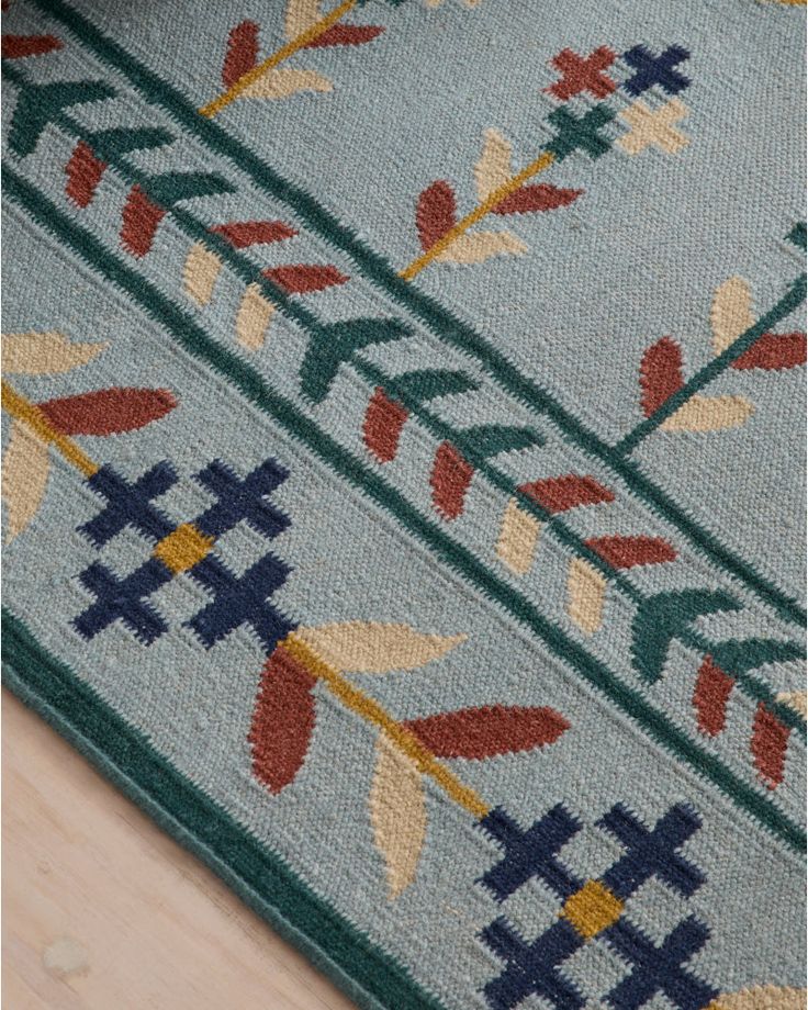 a blue rug with colorful flowers and leaves on the floor next to a wooden floor