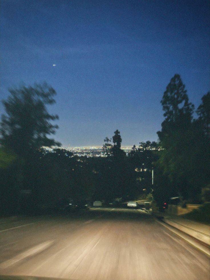 a blurry photo of the street and trees at night with a city in the distance