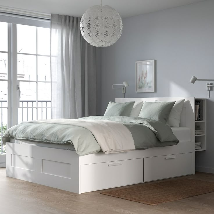 a white bed sitting next to a window in a room with wooden floors and furniture