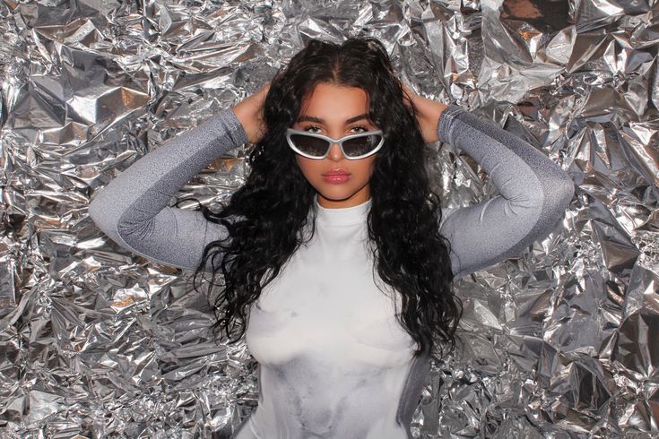 a woman wearing sunglasses standing in front of tinfoiled wall with her hands on her head