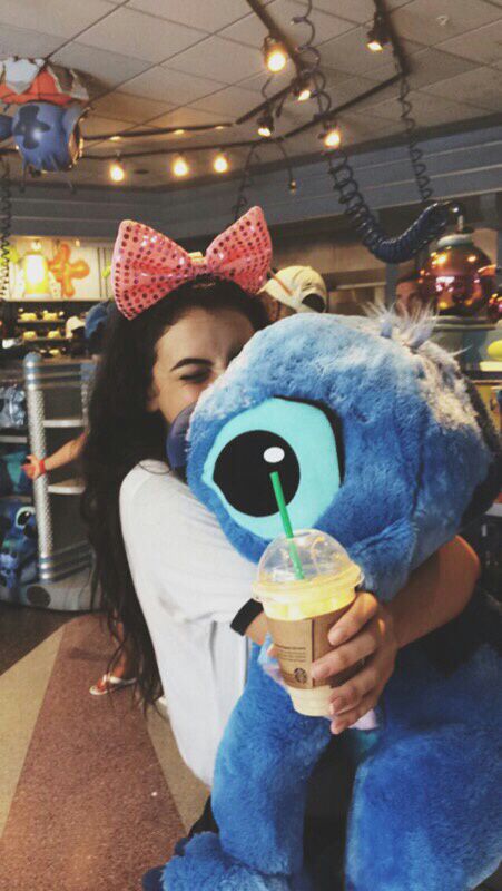 a woman is holding a blue stuffed animal and drinking a drink with a straw in her hand