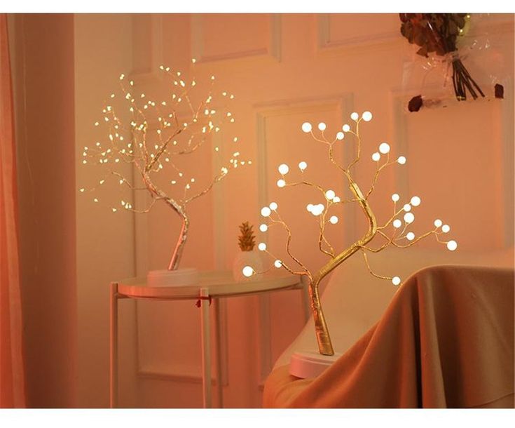 a white table topped with a vase filled with flowers and lights next to a tree