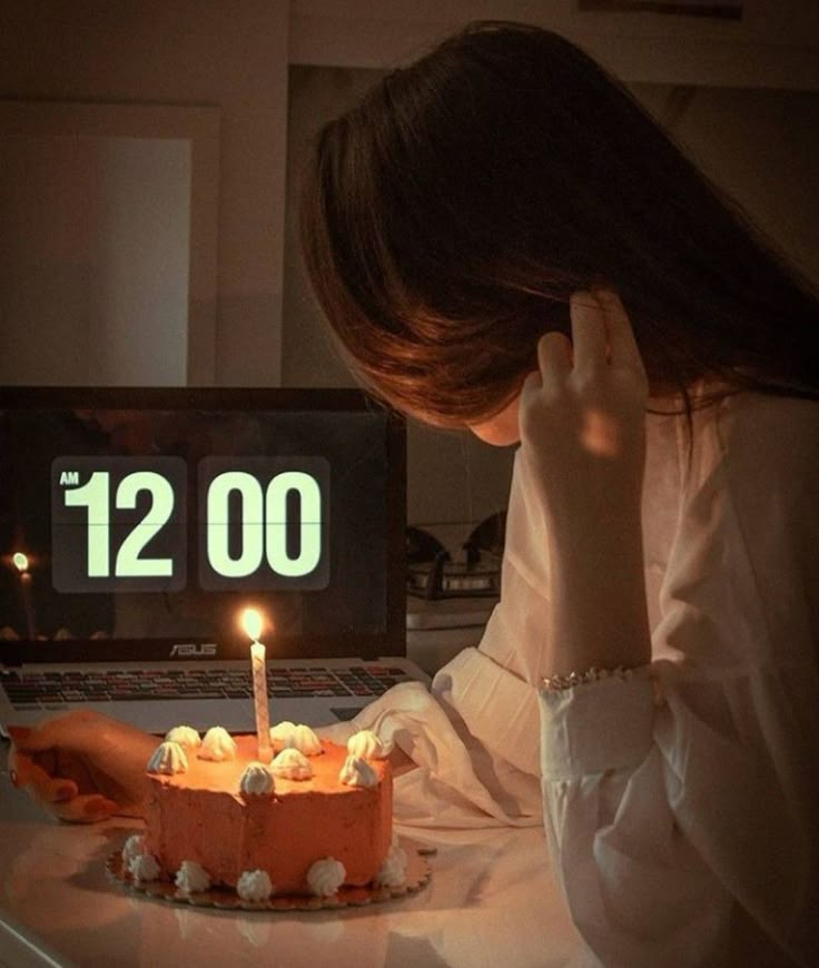 a woman sitting in front of a laptop with a birthday cake on the table next to her