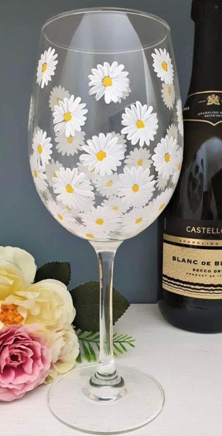 a wine glass with daisies painted on it next to a bottle