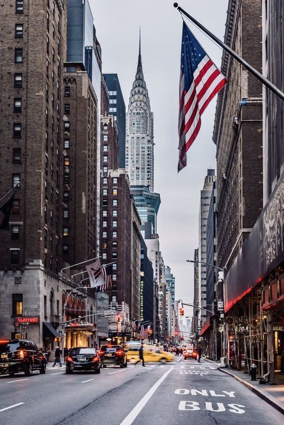 an empty city street with tall buildings and cars driving down the road in front of it