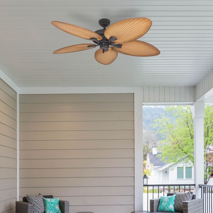 a ceiling fan mounted on the side of a house's wall next to two couches