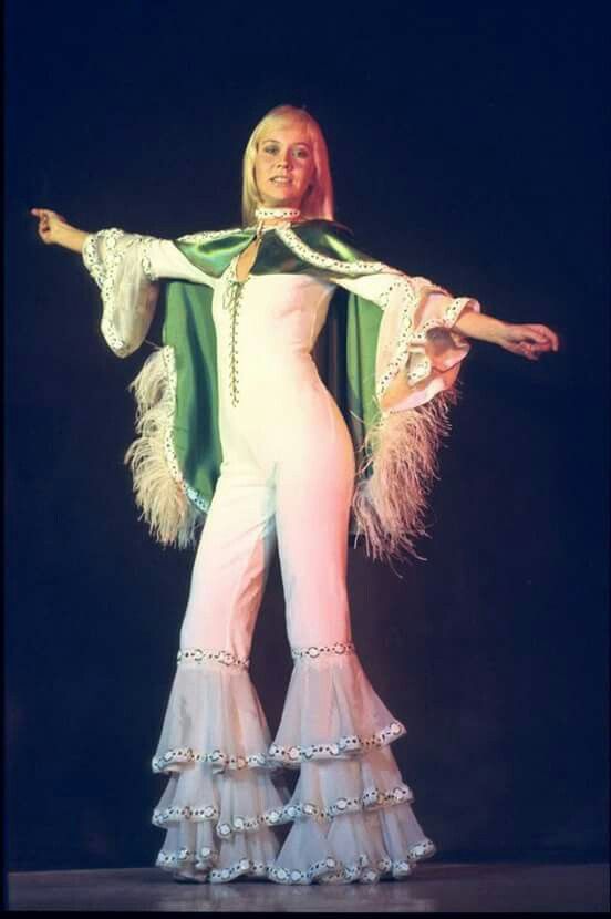 a woman in white and green outfit on stage with her arms spread out to the side