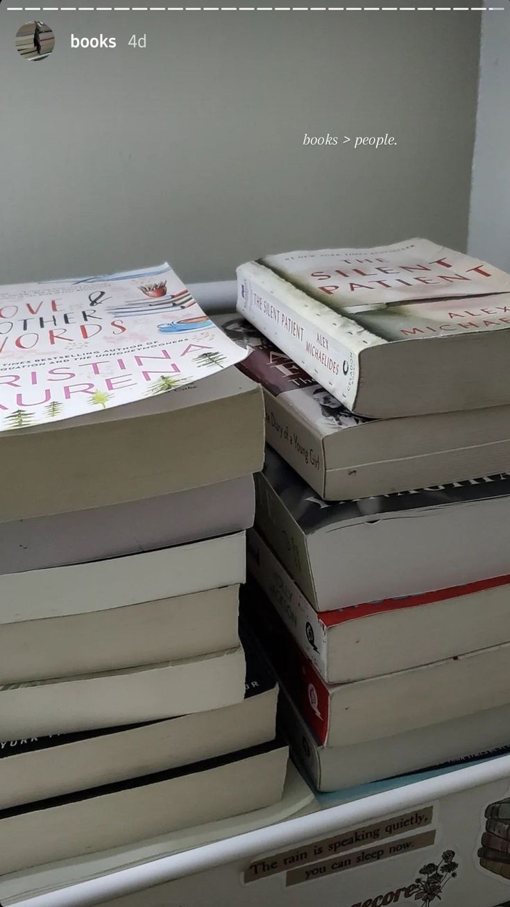 several books stacked on top of each other in front of a white wall and window