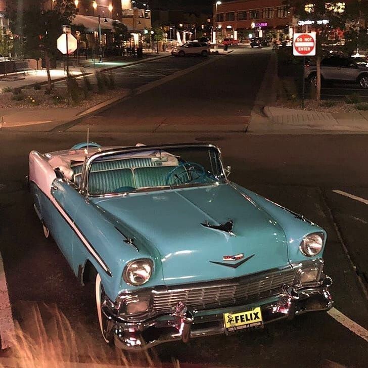 an old blue car is parked on the side of the road at night with its hood up