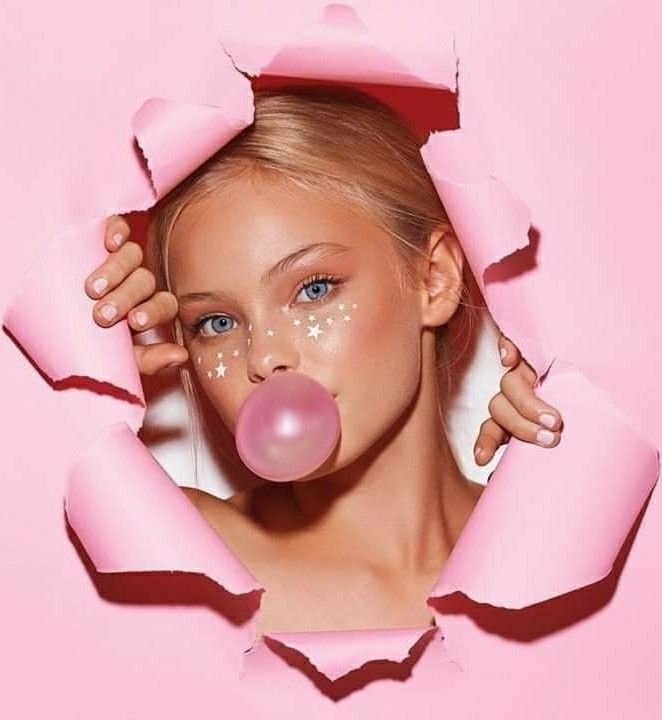 a woman with bubble gums sticking out of her mouth through a hole in pink paper