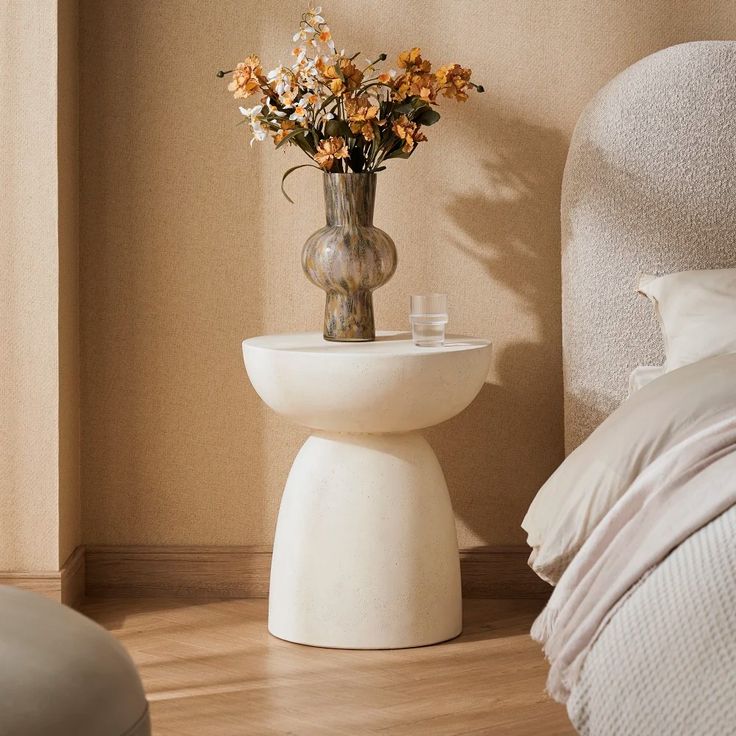 a vase with flowers sitting on top of a white pedestal next to a bed in a bedroom