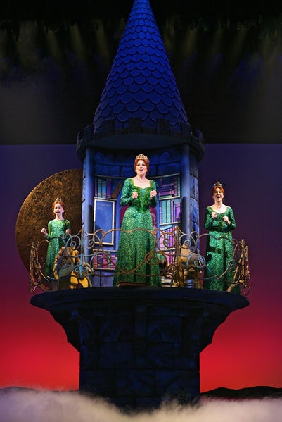 three women in green dresses standing on top of a clock tower with clouds around them