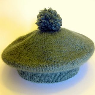 a green knitted hat with a blue pom - pom on the top