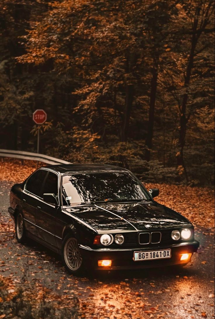 a black car parked on the side of a road in front of trees and leaves