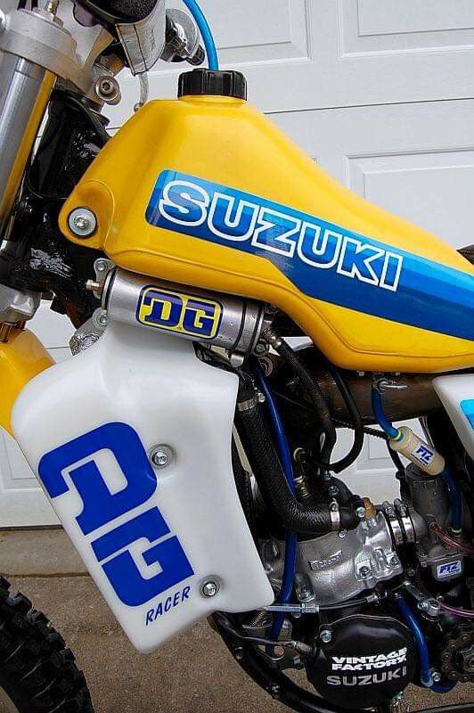 a yellow and blue dirt bike parked in front of a garage door with the words suzuki on it