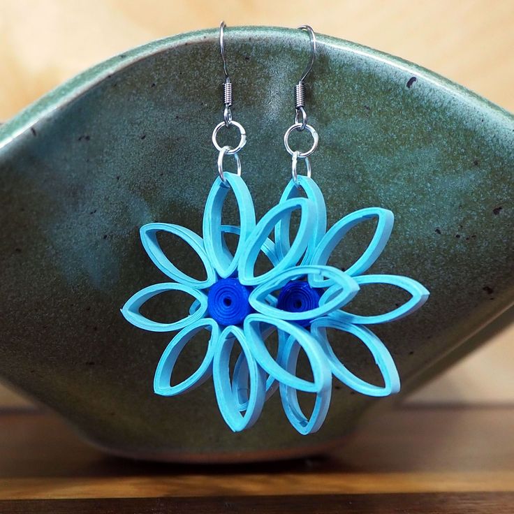 a pair of blue flower earrings sitting on top of a wooden table next to a green bowl