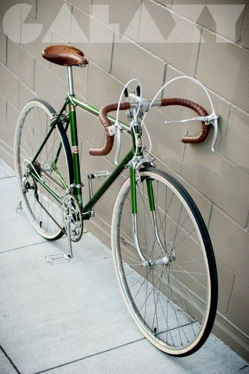 a green and white bicycle parked against a brick wall next to a cement block with a wooden seat on it