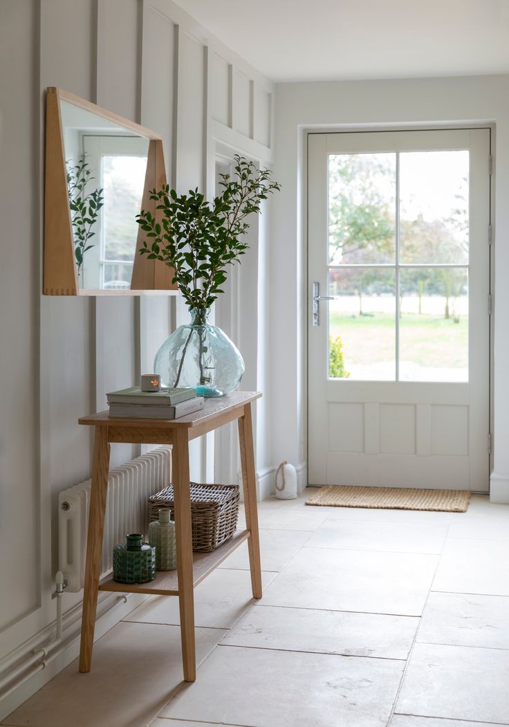 a wooden table with a vase on top of it next to a mirror and door