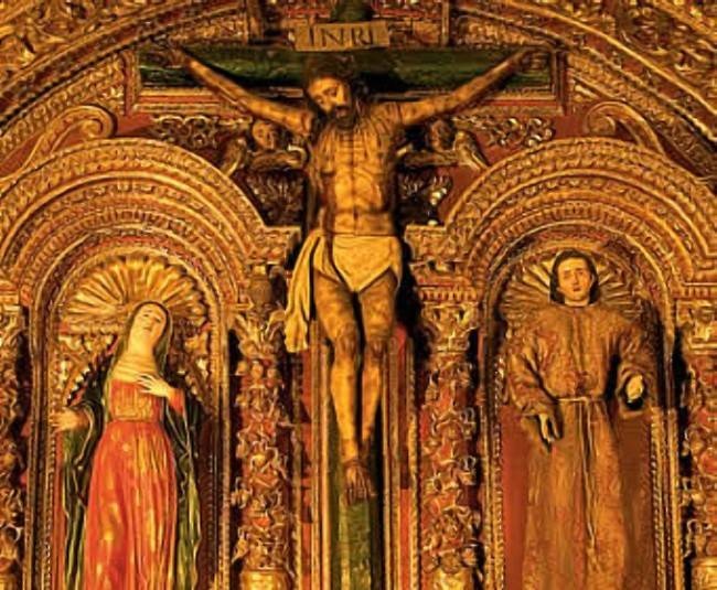 the crucifix is painted gold and has three people standing on top of it