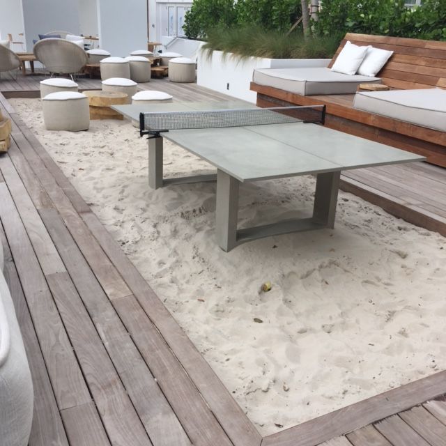 a table sitting on top of a sandy beach next to benches and lounge chairs in the sand