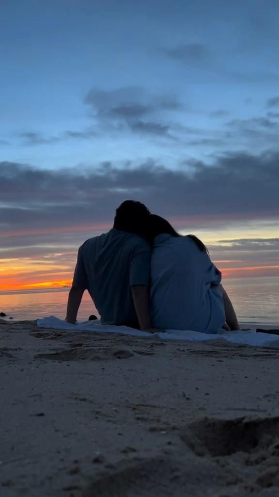 a person sitting on the beach at sunset with their back to the camera, looking into the distance