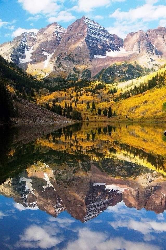 the mountains are reflected in the still waters of this mountain lake, which is surrounded by yellow and green trees