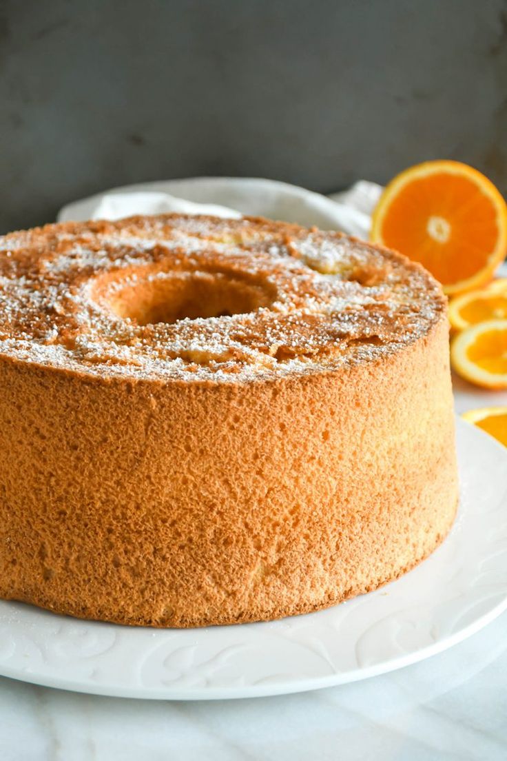 a cake with powdered sugar on top sits on a plate next to sliced oranges