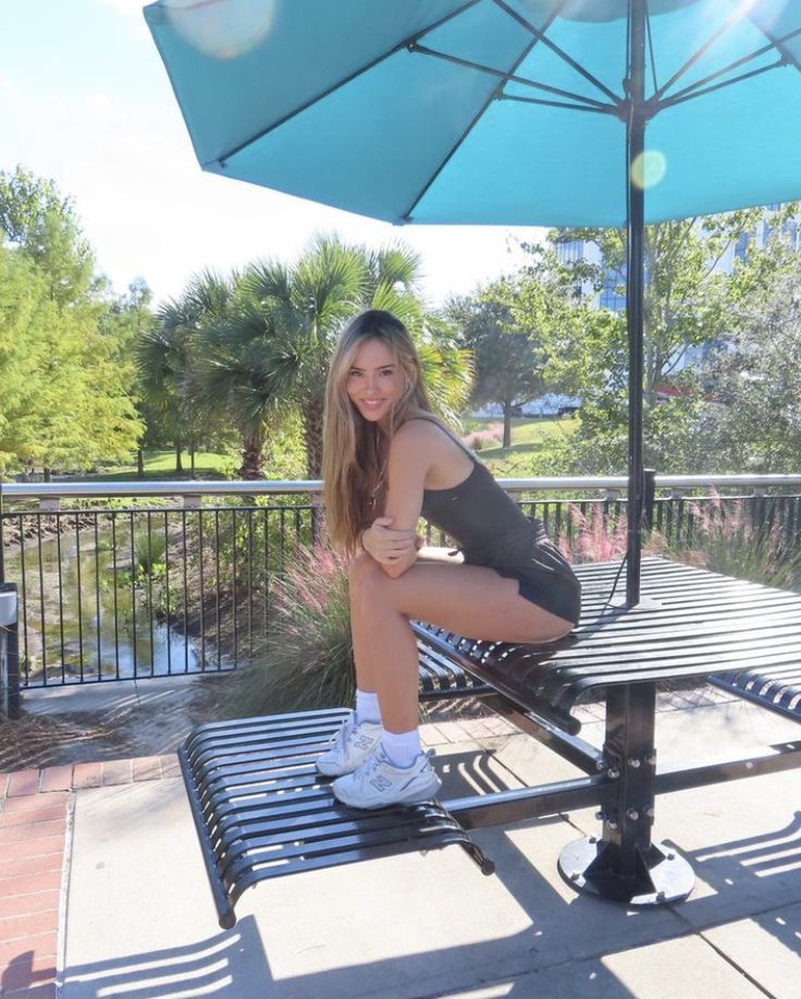 a beautiful young woman sitting on top of a metal bench next to a blue umbrella