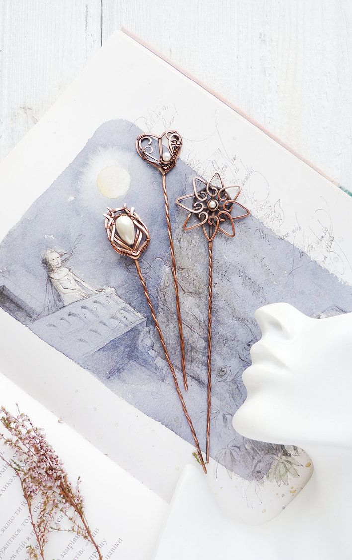 three hair pins sitting on top of an open book next to some flowers and leaves