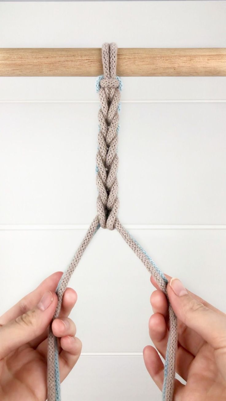 two hands are pulling up the ends of a rope to make a knotted wall hanging