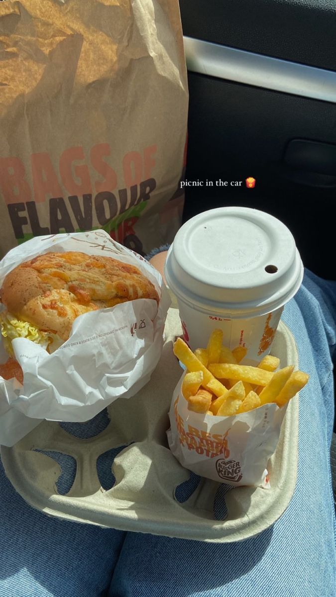 a sandwich and french fries on a tray in the back seat of a car next to a cup of coffee