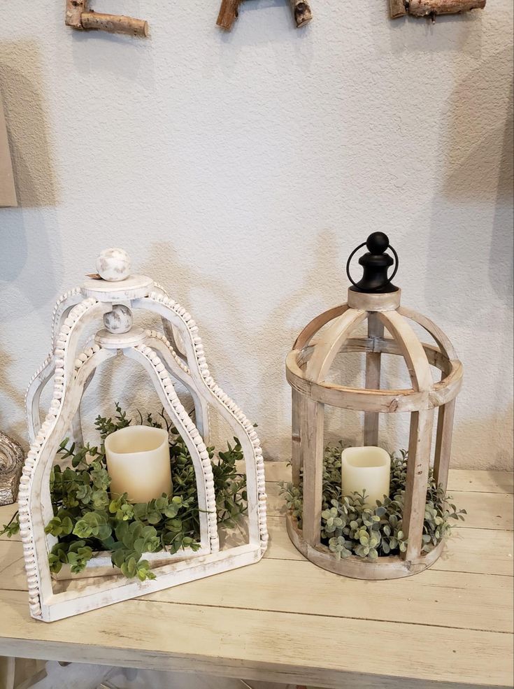 two small white lanterns with candles are on a table