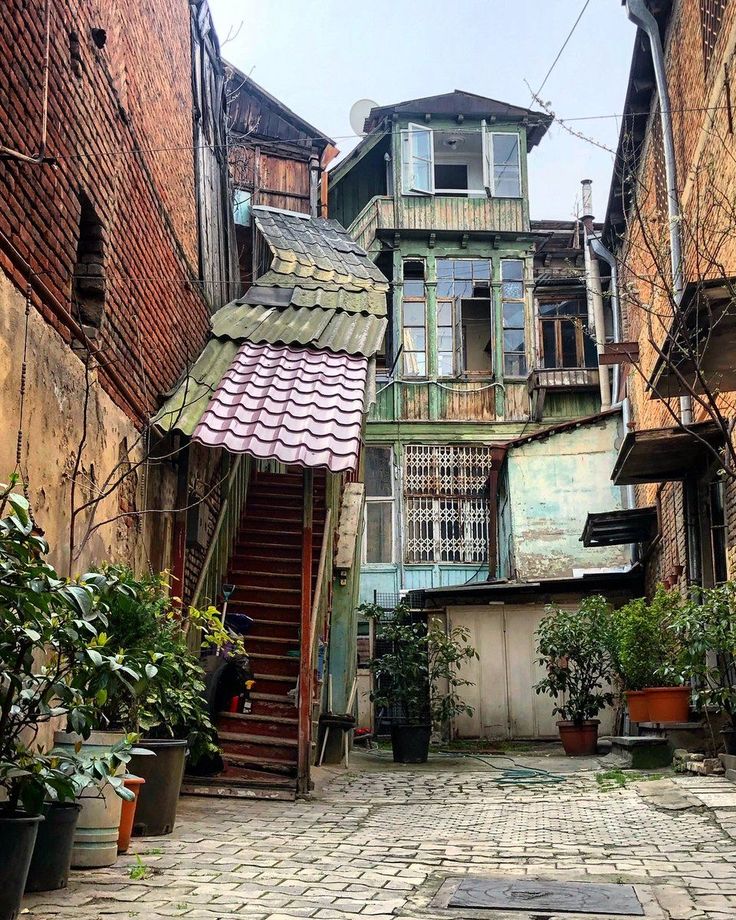 an alleyway with potted plants and stairs leading up to the second story building