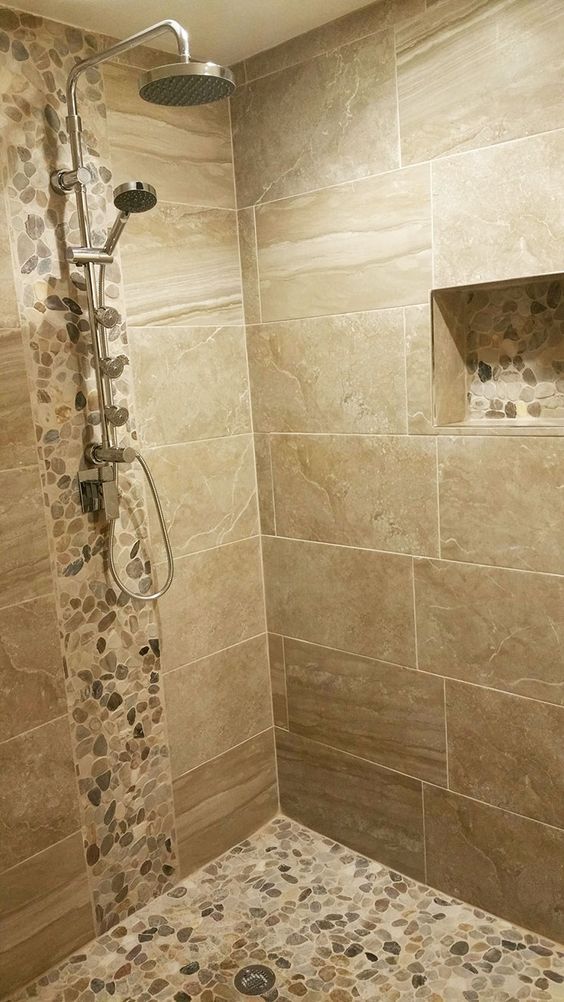 a walk in shower sitting next to a tiled wall and floor with pebbles on it