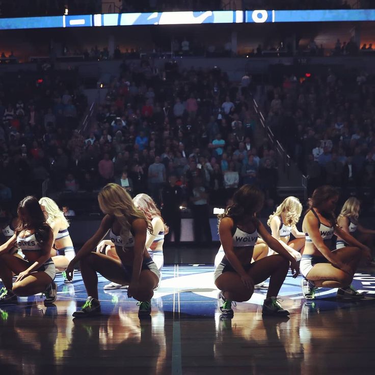 several cheerleaders kneeling down on the floor in front of an audience at a basketball game