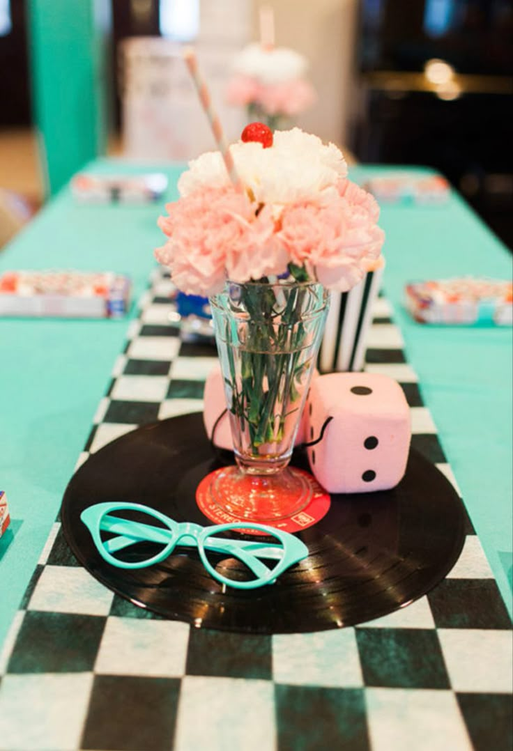 a table topped with a vase filled with flowers next to dice and pink carnations