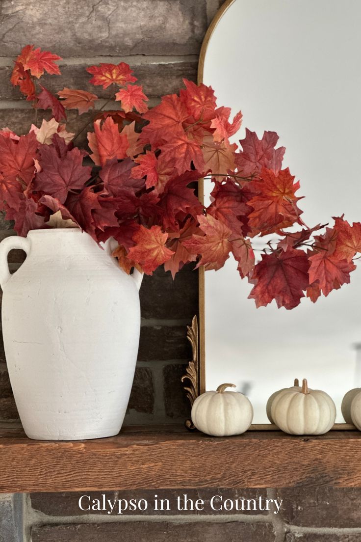 Stone fireplace with gold mirror, white mini pumpkins and red maple leaves in a white vase. Sherwin Williams Naval, Layer Artwork, Elegant Fall Decor, Fall Feeling, Mantel Decorating, Mantel Ideas, Fall Vignettes, Fireplace Mantel Decor, Fall Front Porch Decor