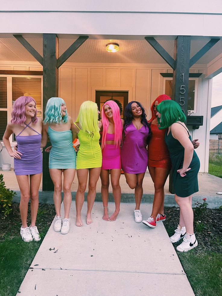 four women dressed in colorful wigs are standing on the sidewalk and posing for a photo