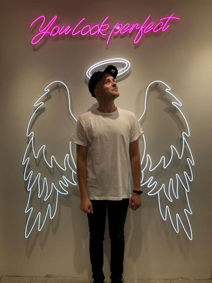 a young man standing in front of a neon sign with an angel wings on it