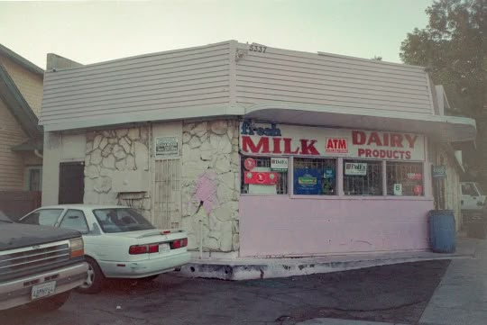 an old milk shop with cars parked in front and the building has peeling paint on it