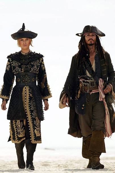 two people dressed in pirate costumes walking on the beach with one person wearing a hat